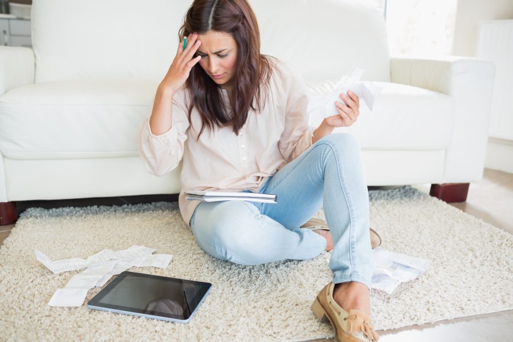 Woman surround by papers and a computer tablet, looking distressed