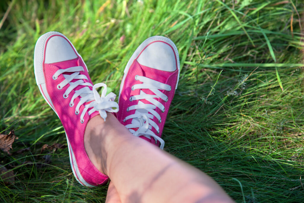 A woman's legs in the grass with pink canvas shoes like Converse.