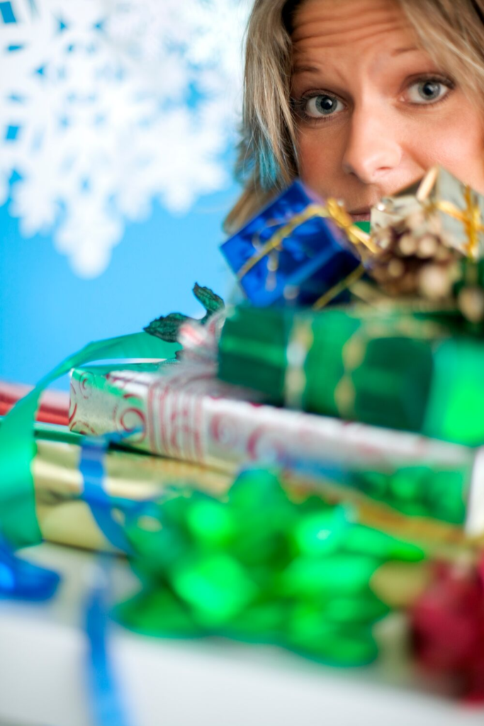 Woman holding a pile of Christmas gifts, looking overwhelmed