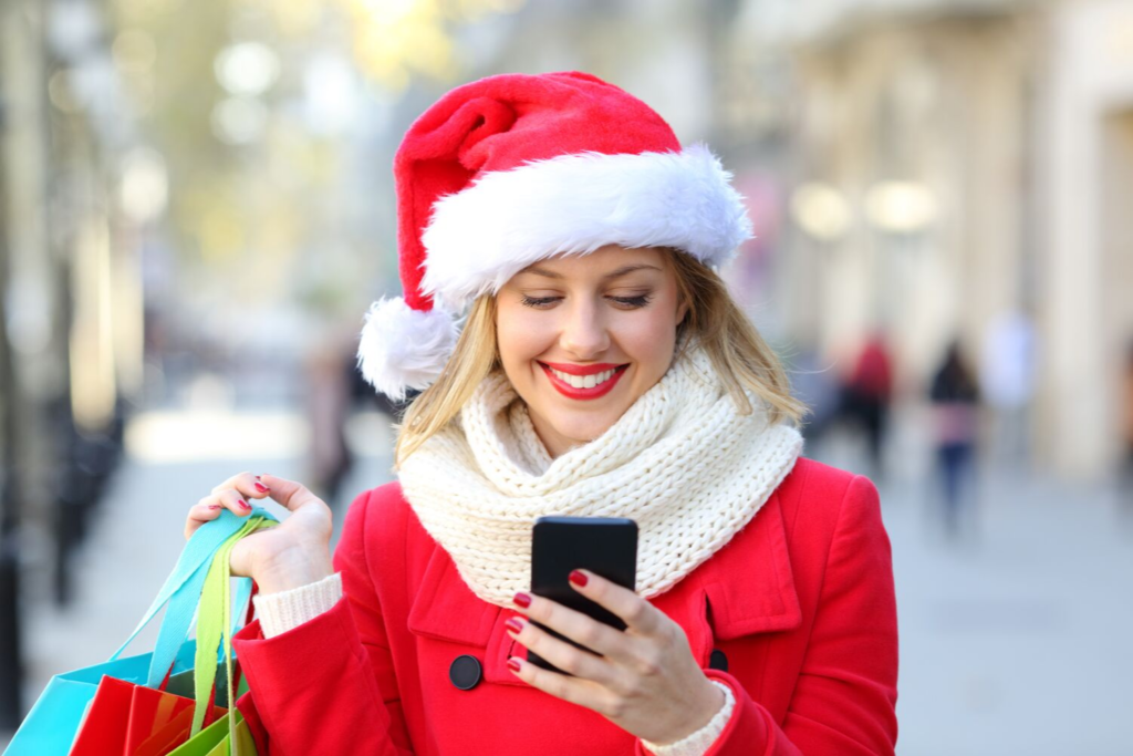 Woman smiling at phone while holding Christmas shopping bags